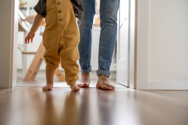 Küçük çocuk evde babasının yanında yürümeyi öğreniyor.