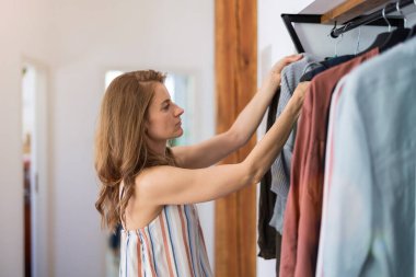 Genç bir kadın evdeki gardırobundan kıyafetlerini karıştırıyor.