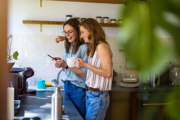 Dvě Ženy Používají Mobilní Telefon Kuchyni Doma — Stock fotografie