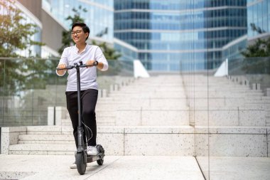 Şehir merkezinde elektrikli scooter kullanan genç bir adam.