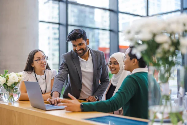 A diverse group of business people gather around a laptop in a modern office