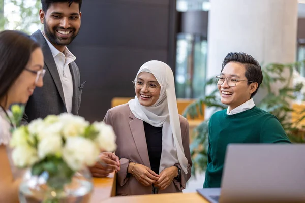 A diverse group of business people gather around a laptop in a modern office