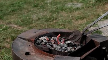 Yakın plan bir demirci, erimiş kırmızı metal bir nalı maşayla ateşe çevirir. Demircilik teknesi..