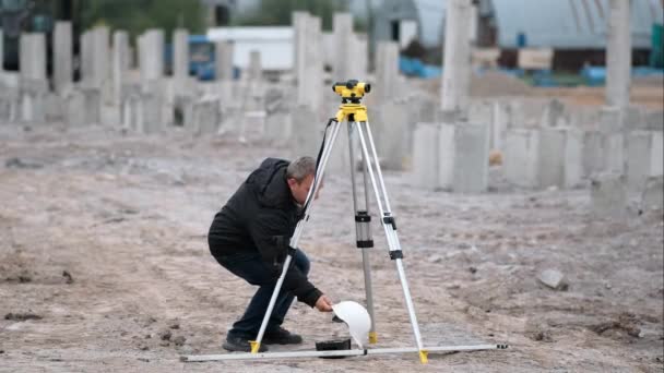 Siwy Mężczyzna Białym Hełmie Spogląda Żółty Teodolit Placu Budowy Pomiary — Wideo stockowe