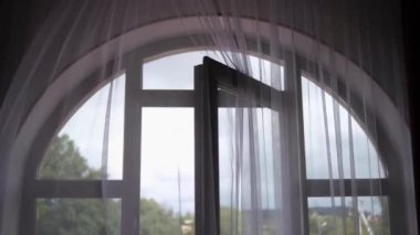 Doğanın balkondan görünüşü. Rüzgarda hafif bir tül sallanıyor. Pencere ve kapıda şeffaf bir perde var. Rüzgâr tarafından hafifçe sallanıyor..