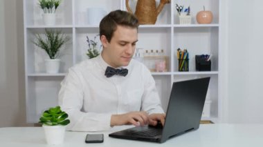 Genç bir adam ofisinde masasında oturuyor ve laptopuyla çalışıyor..