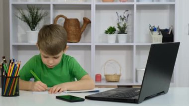 Küçük bir çocuk bir odada bir masada oturuyor ve bir dizüstü bilgisayar kullanarak ödev yapıyor. Mutlu çocukluk kavramı.