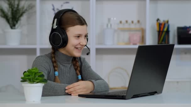 女の子は机の上に座り ノートパソコンとヘッドフォンで通信します 自己分離に関する学校での学習 — ストック動画