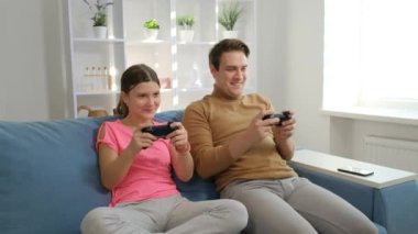 Genç bir oğlan ve bir kız, kız ve erkek kardeş, kanepede oturmuş ellerinde joysticklerle oyun oynuyorlar. Her ailede alet kavramı.