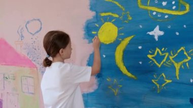Küçük bir kız, pembe duvar kağıdındaki bir apartmanın duvarına güneşi ve yıldızları çiziyor. Mutlu bir çocukluk ve sanat aşkı kavramı..