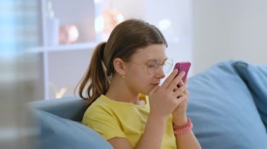 Kanepede oturmuş akıllı telefonuna yakından bakan gözlüklü genç bir kız. Görüş sorunları.