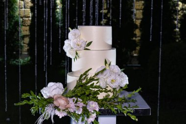 Gece düğün kemerinin önünde beyaz çiçeklerle süslenmiş güzel düğün pastası..