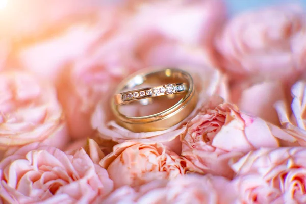 Wedding gold rings with diamonds on pink roses close-up.