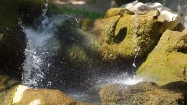 A naturally beautiful waterfall among the rocks in the forest on a summer sunny day. Close-up. Slow motion.