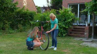 Anne, evin arka bahçesinde kızının bisikletini tamir etmesine yardım eder. Mutlu, dost canlısı, düşünceli anne..