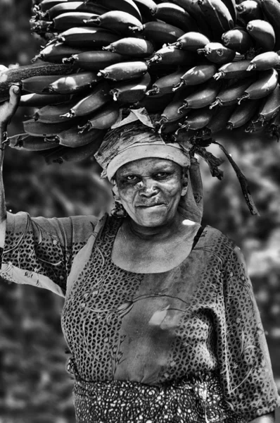 Een vrouw met banana's cluster op haar hoofd, op de weg naar de markt voor bananen in marangu dorp, tamzania. — Stockfoto