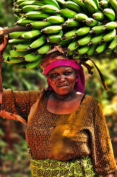 Женщина, несущая скопление бананов на голове, на пути к банановому рынку в деревне Марангу, Танзания . Лицензионные Стоковые Фото