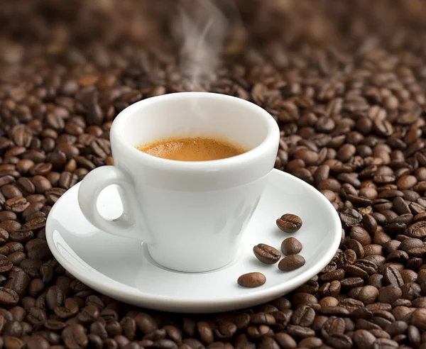 Steaming cup of coffee on background of coffee beans — Stock Photo, Image