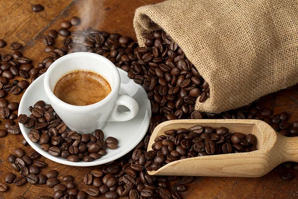 Coffee cup with jute bag and spoon full of coffee beans — Stock Photo, Image