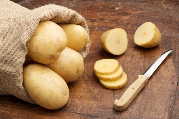 Rohe Kartoffeln und Fnife auf einem hölzernen Hintergrund — Stockfoto
