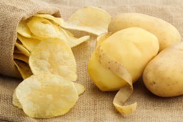 Chips und geschälte Kartoffeln auf Jute-Textur — Stockfoto
