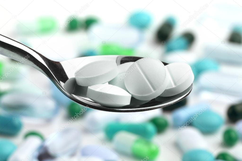 Spoon full of tablets over a background of assorted medicines