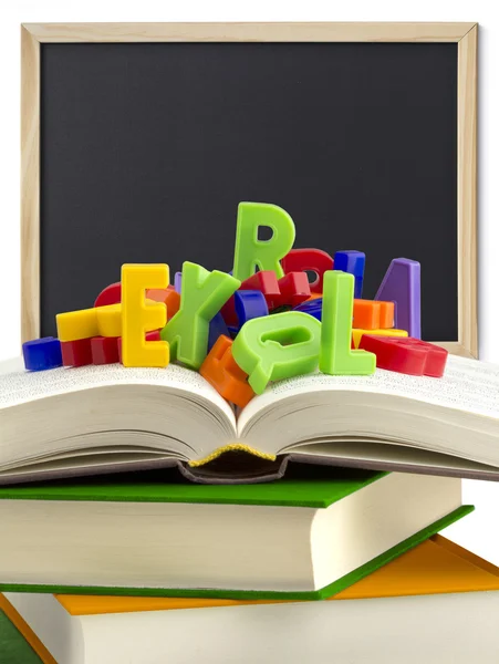 Stack of books, colored letters and a blackboard in the background — Stock Photo, Image