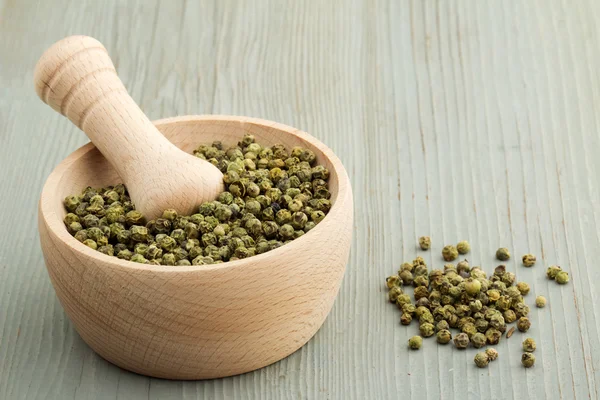 Mortar and pestle with green peppercorns on wooden table — Stock Photo, Image