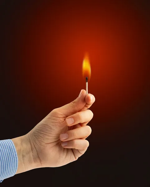 Hand holding a burning matchstick on dark red background — Stock Photo, Image