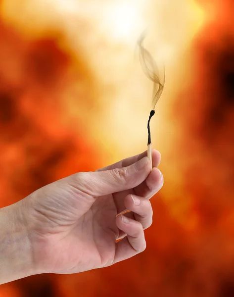 Hand holding an extinguished matchstick on a fiery background — Stock Photo, Image