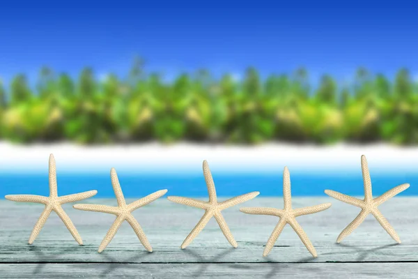 Cinco estrellas de mar sobre mesa de madera en paisaje tropical —  Fotos de Stock