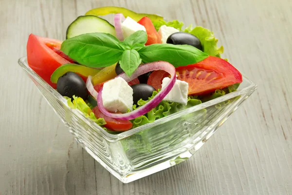 Свежий греческий салат в стеклянной миске на деревянном столе — стоковое фото