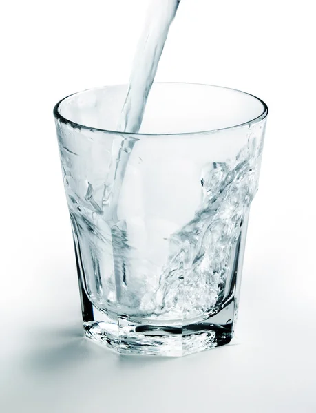 Getto d'acqua riempire un bicchiere su sfondo bianco — Foto Stock