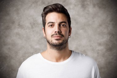 Sakallı ve küpeli genç adam kameraya özgüvenle bakıyor.