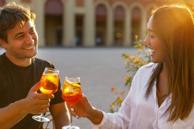 Genç çift gün batımında aperol spritz ile gülüyor ve kadeh kaldırıyor. 