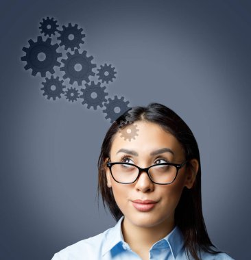Portrait of young woman wearing glasses looking up at cogwheels isolated on grey background. New ideas and startup concept.