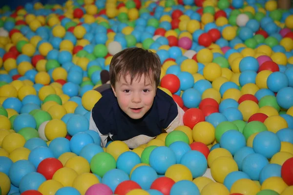 Een vrolijke jongen speelt in de speelkamer in het zwembad met ballen van verschillende kleuren — Stockfoto