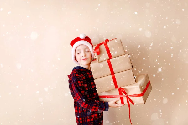 Malý chlapec s vánočním kloboukem a vánočními dárky. Pozdrav. Koncept zimních prázdnin. — Stock fotografie