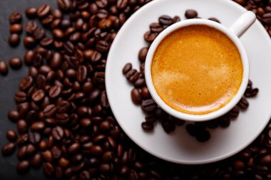 Sabah menüsü için süt köpüklü sıcak sade kahve beyaz seramik bardakta kahve çekirdekleri kavrulmuş.