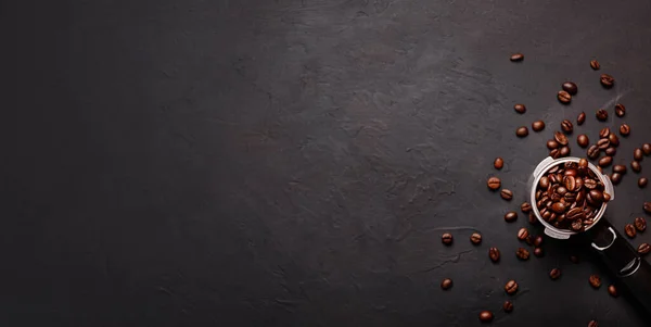 Horizontal banner with cup of coffee and coffee beans on dark stone background. Top view. Copy space