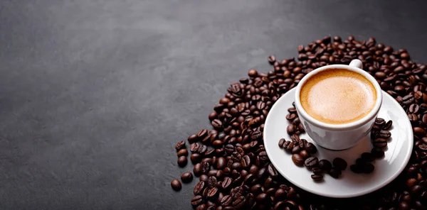 Horizontal banner with cup of coffee and coffee beans on dark stone background. Top view. Copy space