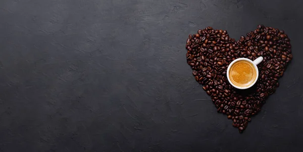 Horizontal banner with cup of coffee and coffee beans on dark stone background. Top view. Copy space