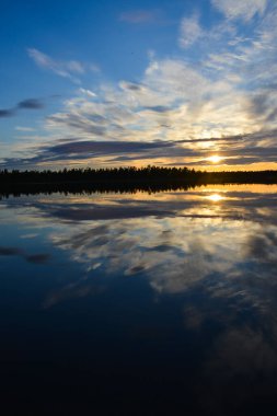 Yaz gündönümü sırasında Finlandiya, Laponya 'daki bir göle yansıyan gece yarısı güneşi.