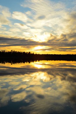 Yaz gündönümü sırasında Finlandiya, Laponya 'daki bir göle yansıyan gece yarısı güneşi.