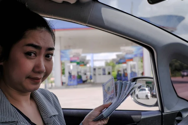 Desperate women hold cash dollar bills next to the car with an open tank, concept of rising fuel prices