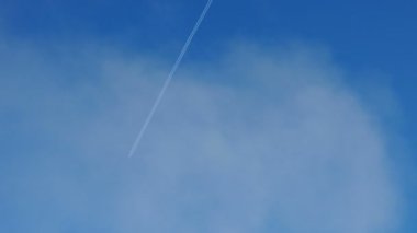Mavi gökyüzünde uçan uçağın izi. Mavi gökyüzünde beyaz bulutlar. Buhar izi.