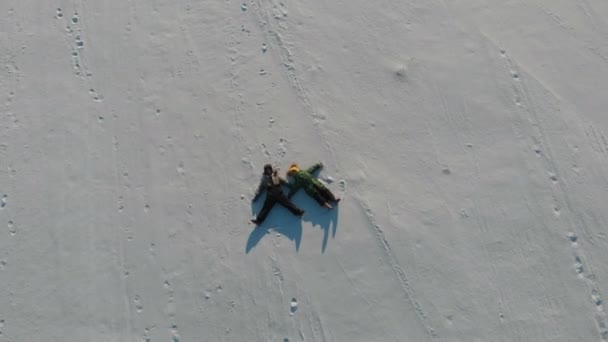 Ryssland, Saratov - Jan, 2021: Två barn skildrar snöänglar som ligger på nysnö i form av ett kors. glad och energisk, med stänk av snö. — Stockvideo