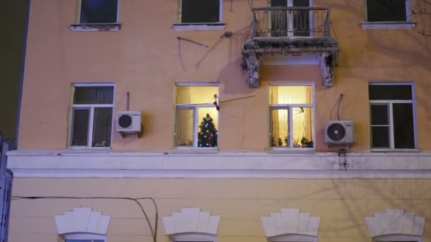 Saratov, Rússia - janeiro de 2022: Natal e Ano Novo. Cena noturna com árvore de Natal decorada brilhando em um quarto da casa privada, vista do exterior — Vídeo de Stock