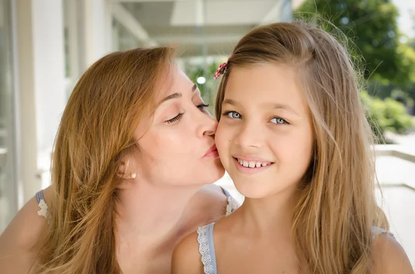 Mother kissing her daughter in the cheek.