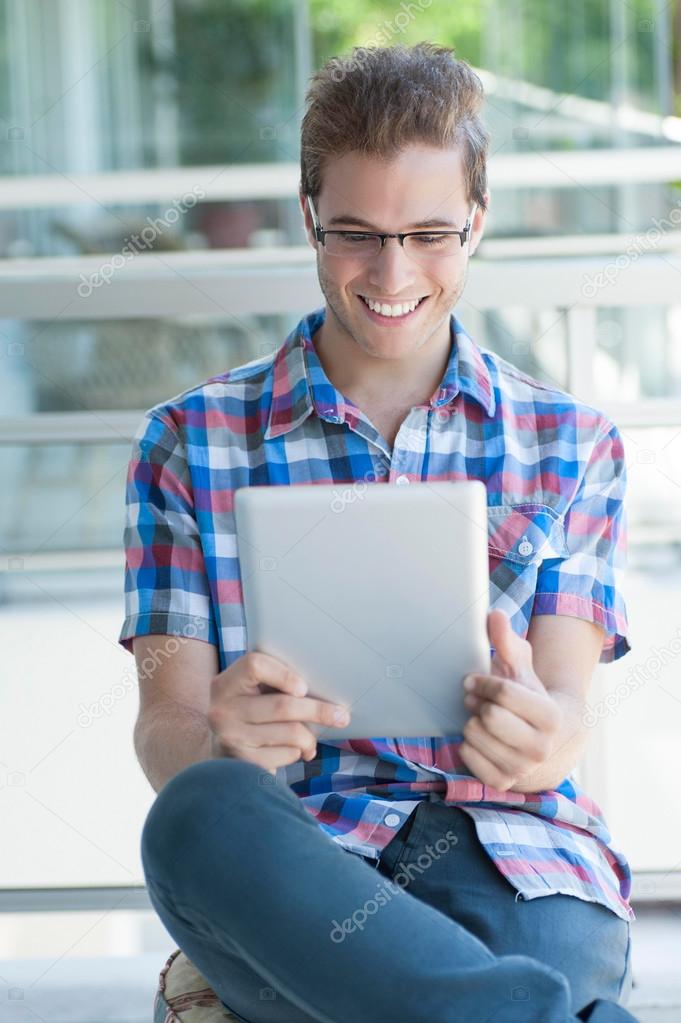 Young smiley male using tablet pc wearing reading glasses